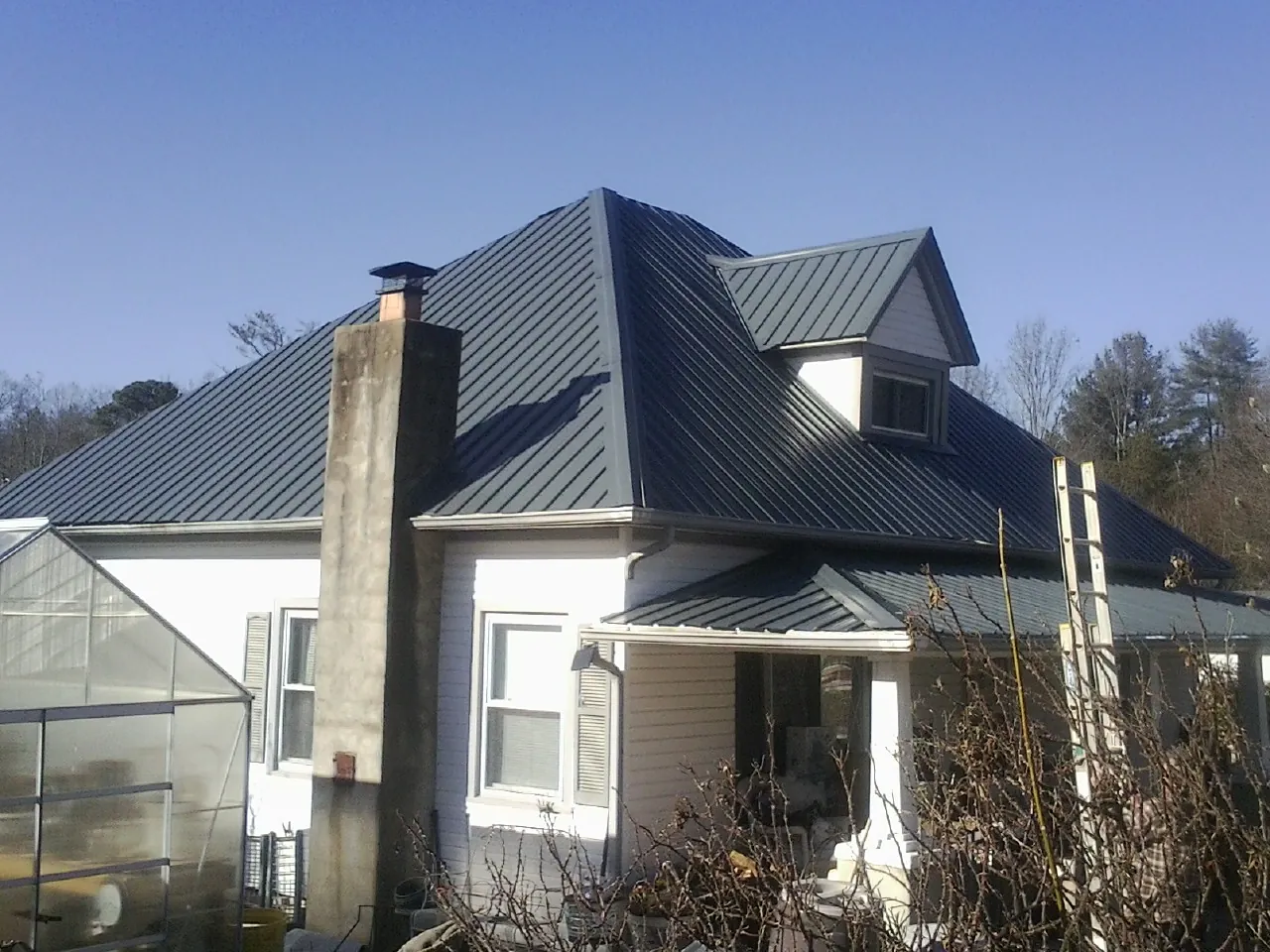 Dark blue standing seam metal roof on a white farmhouse with dormer — Slate & Tile Roof Repair by Roofing Brothers in Mount Royal