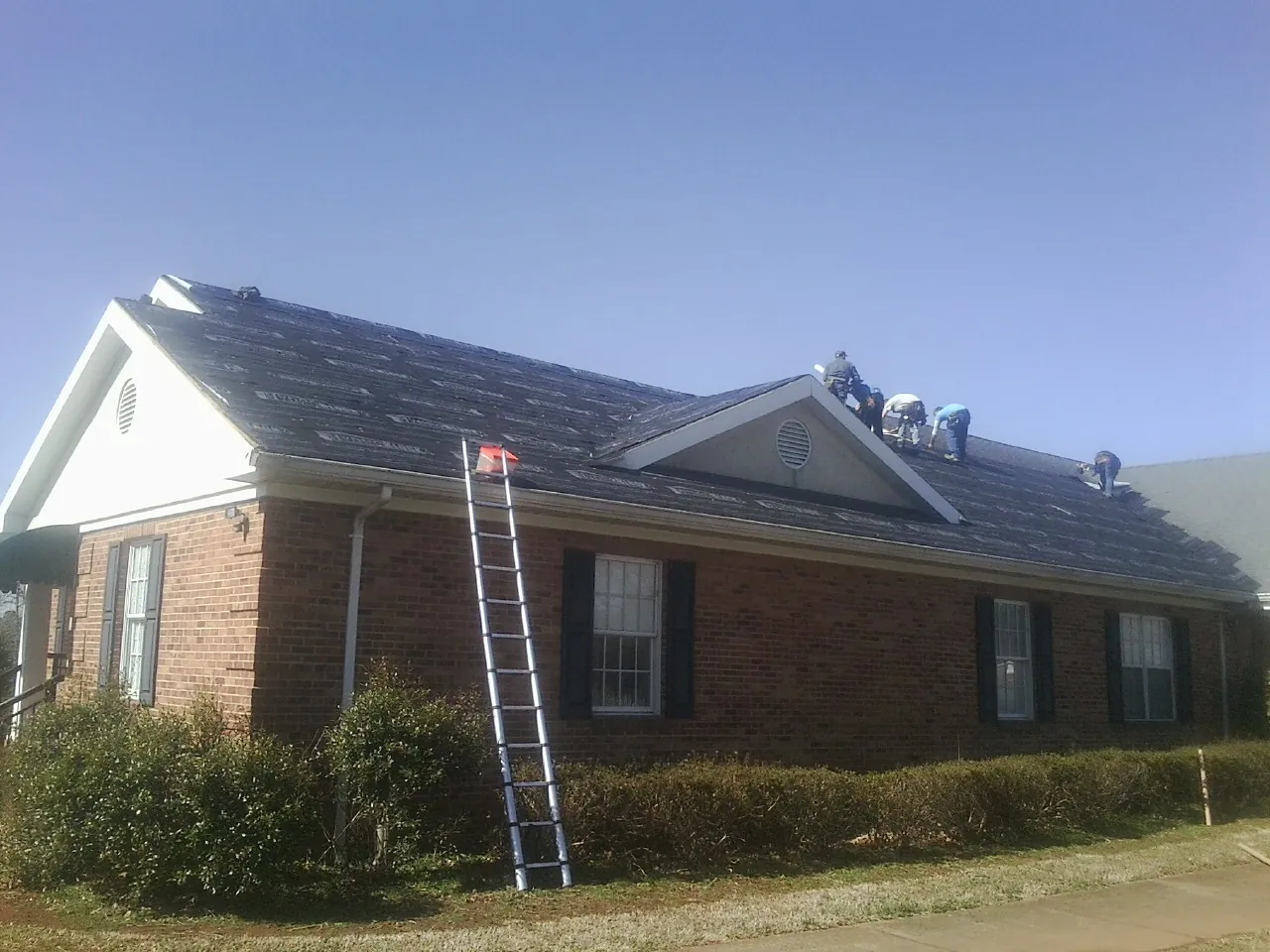 Crew tearing shingles off a brick ranch roof with a ladder set — Emergency Roof Repair work by our crew in Mount Royal