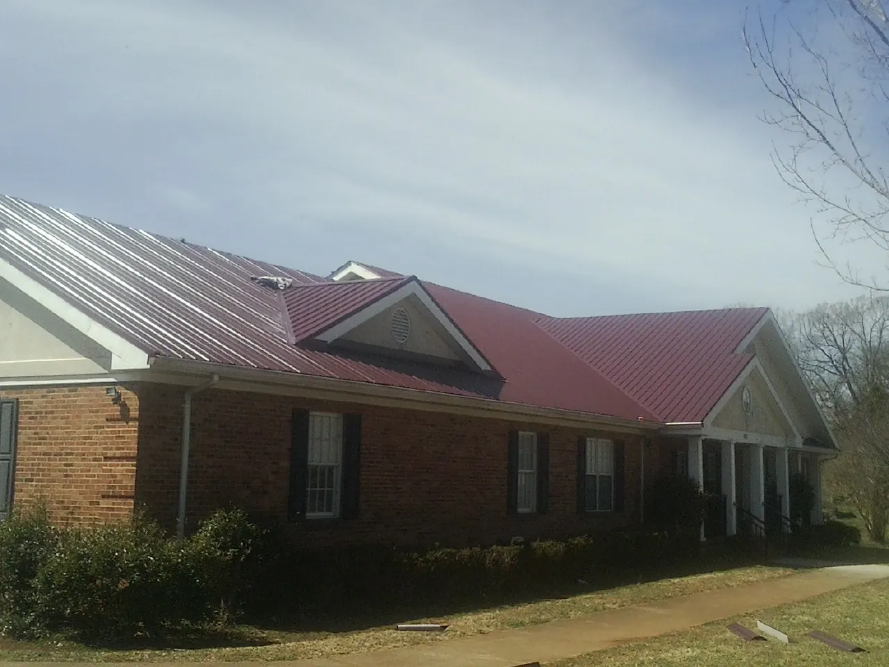 Red metal roof with gabled entries on a long brick building, from a Hail Damage Roof Repair job in Mount Royal