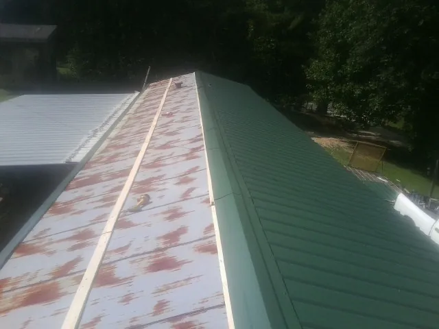 Old rusted panels beside newly installed green metal roofing — Wind Damage Roof Repair by Roofing Brothers in Mount Royal