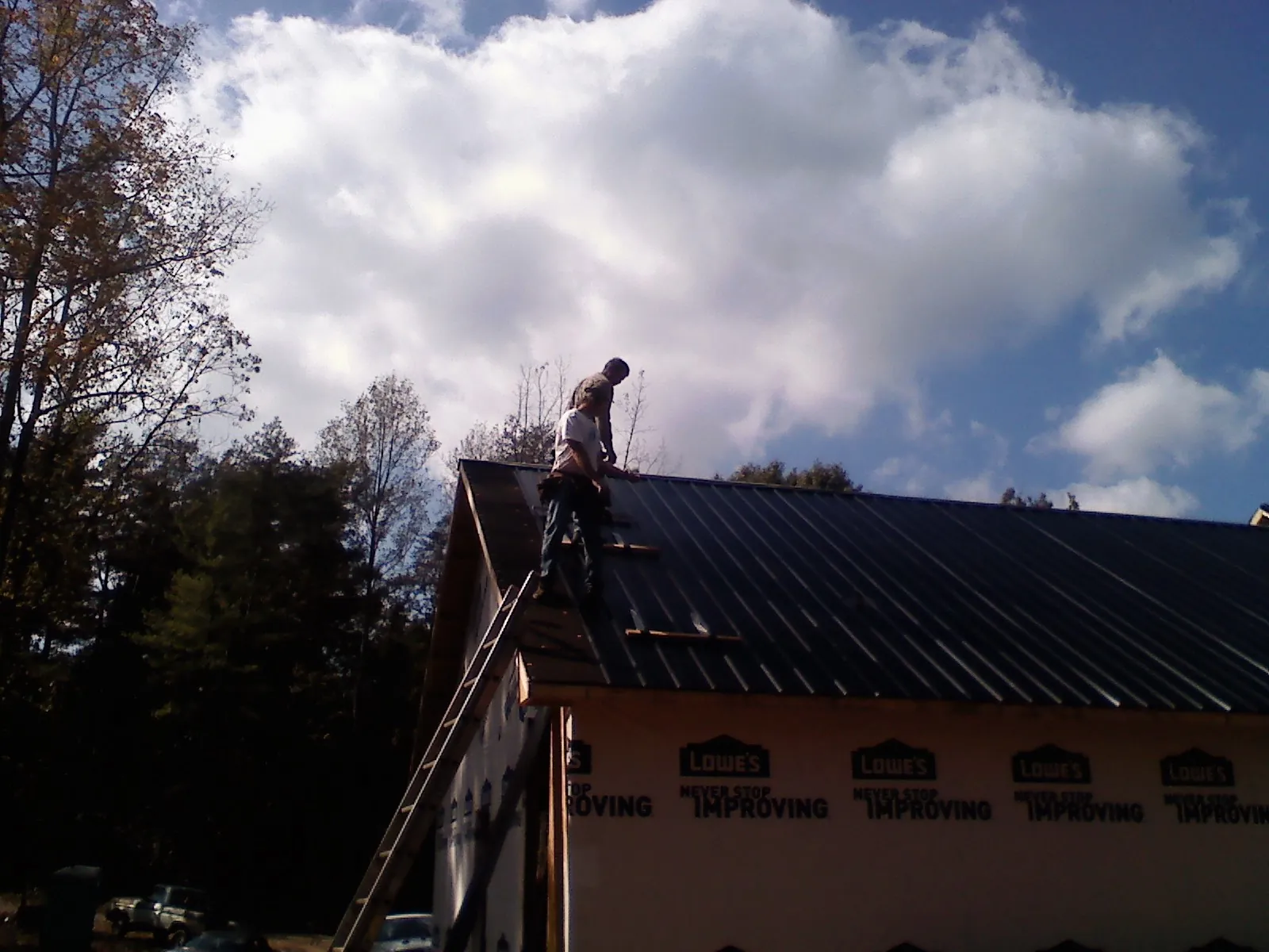 Roofer fastening dark metal panels high against a cloudy sky, from a Roof Inspection job in Mount Royal